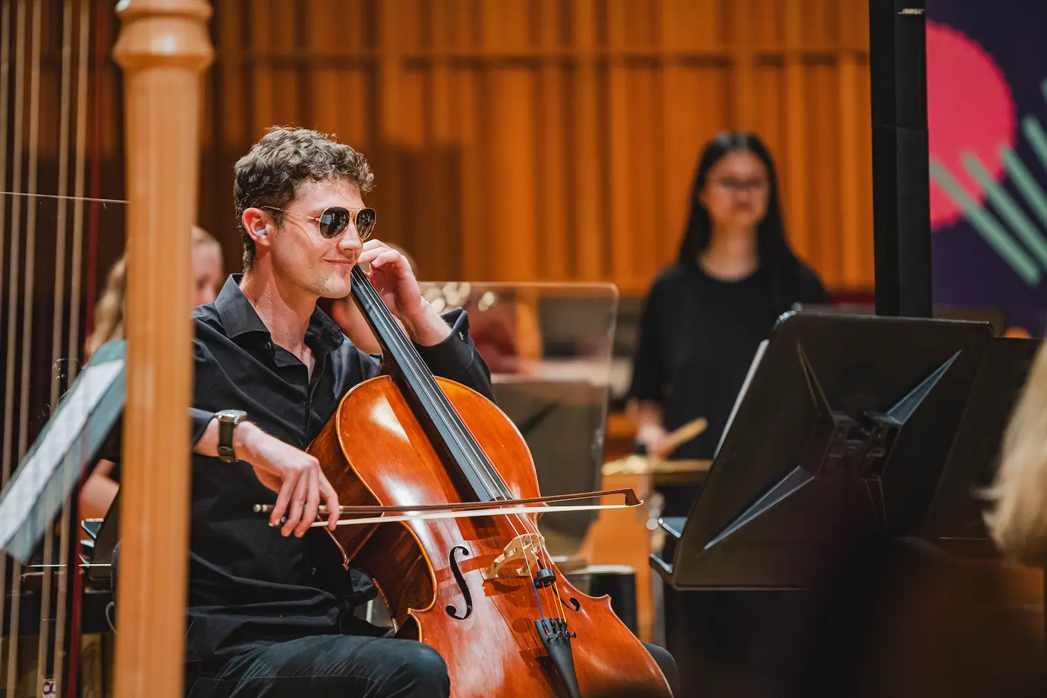 A young musician wearing sunglasses plays cello onstage with the National Open Youth Orchestra (NOYO).